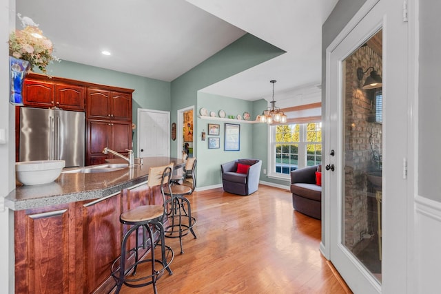 kitchen with high end refrigerator, a sink, baseboards, a kitchen breakfast bar, and light wood-type flooring