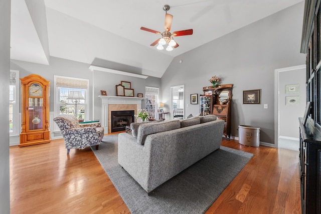 living room with light wood finished floors, baseboards, a ceiling fan, a fireplace, and high vaulted ceiling