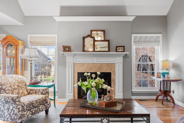 living room featuring a tiled fireplace, wood finished floors, visible vents, and baseboards