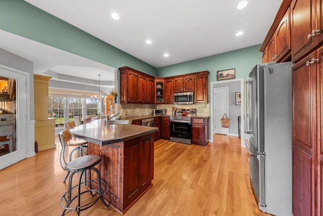 kitchen with stainless steel appliances, a breakfast bar, a peninsula, light wood-style floors, and backsplash