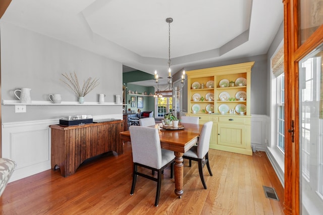 dining room with a decorative wall, a wainscoted wall, a notable chandelier, visible vents, and light wood-style floors