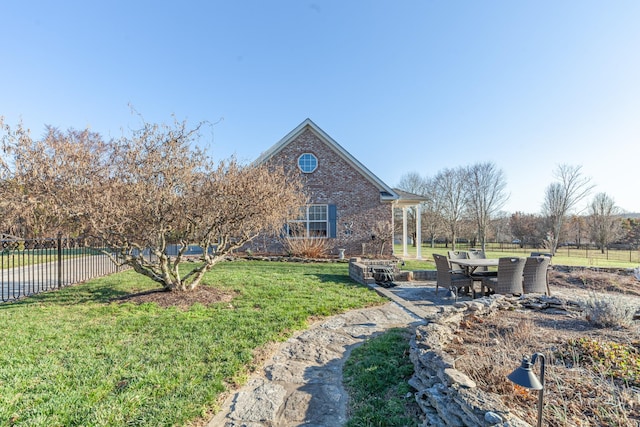 exterior space featuring brick siding, a lawn, a patio area, and fence