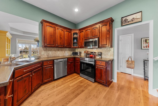 kitchen with appliances with stainless steel finishes, a sink, light wood finished floors, and tasteful backsplash