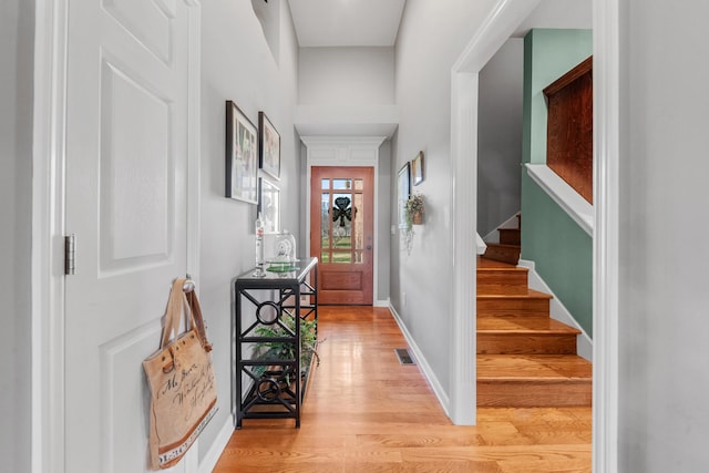 foyer entrance featuring light wood finished floors, baseboards, stairs, and visible vents