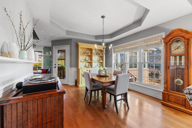 dining area featuring wood finished floors, a raised ceiling, a wealth of natural light, and a notable chandelier