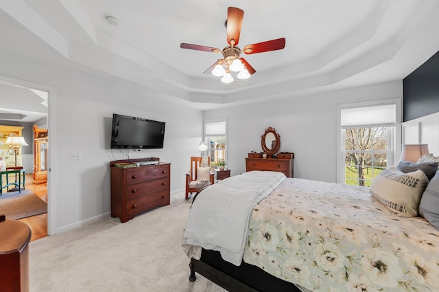 bedroom featuring baseboards, a tray ceiling, a ceiling fan, and light colored carpet