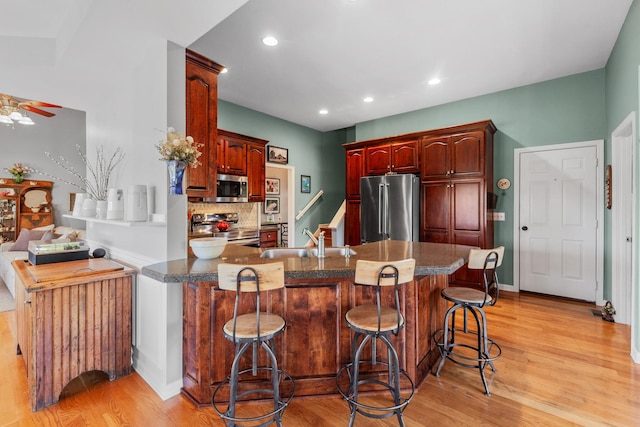 kitchen with reddish brown cabinets, stainless steel appliances, a sink, light wood-type flooring, and a peninsula