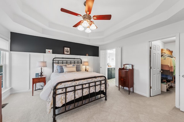 bedroom with ensuite bath, a raised ceiling, a walk in closet, and light colored carpet