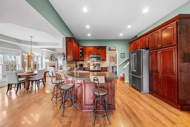 kitchen with stainless steel appliances, a peninsula, a kitchen breakfast bar, light wood-style floors, and tasteful backsplash