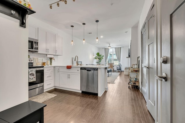 kitchen featuring decorative backsplash, appliances with stainless steel finishes, dark wood-style flooring, a peninsula, and white cabinetry