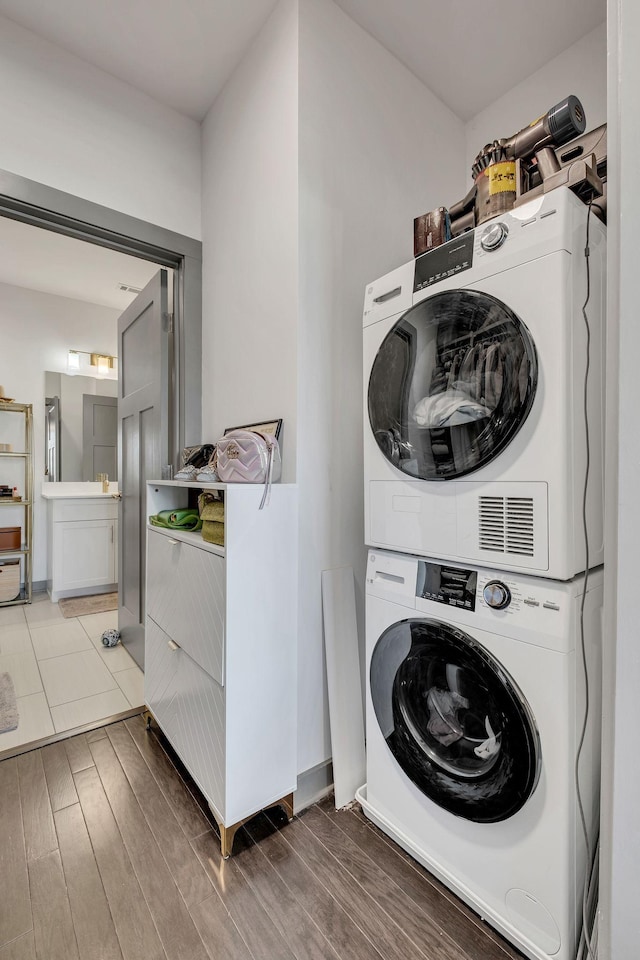 clothes washing area featuring laundry area, stacked washer and clothes dryer, and wood finished floors