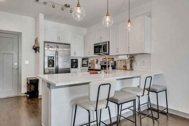 kitchen featuring a peninsula, tasteful backsplash, appliances with stainless steel finishes, and dark wood-style flooring