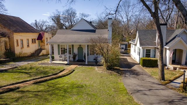 view of front of home with aphalt driveway, a front yard, a porch, and a chimney