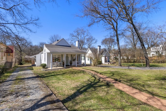 view of front facade featuring a front yard, covered porch, driveway, and a chimney