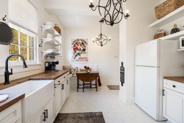 kitchen featuring a notable chandelier, butcher block counters, a sink, freestanding refrigerator, and open shelves