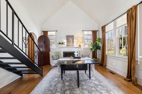 office space featuring a fireplace, visible vents, wood finished floors, high vaulted ceiling, and baseboards