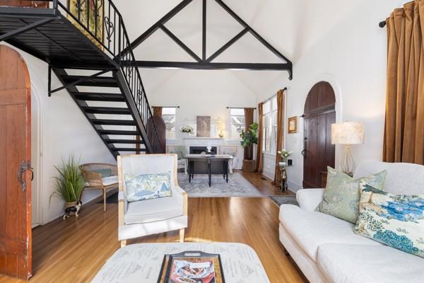 living room with arched walkways, high vaulted ceiling, wood finished floors, and stairs