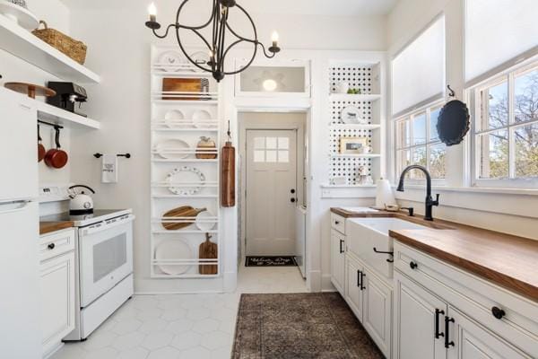 kitchen with a notable chandelier, white appliances, butcher block counters, a sink, and open shelves