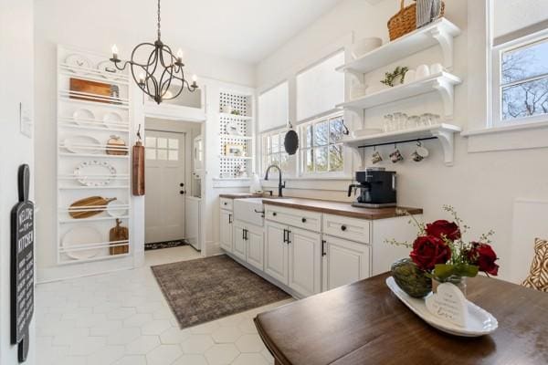 interior space with decorative light fixtures, open shelves, an inviting chandelier, white cabinets, and a sink