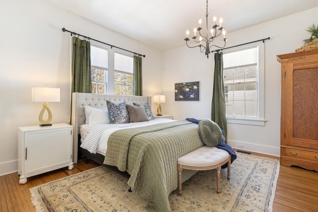 bedroom with an inviting chandelier, visible vents, baseboards, and wood finished floors