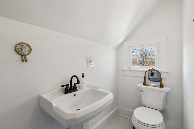 half bathroom with vaulted ceiling, a sink, toilet, and baseboards