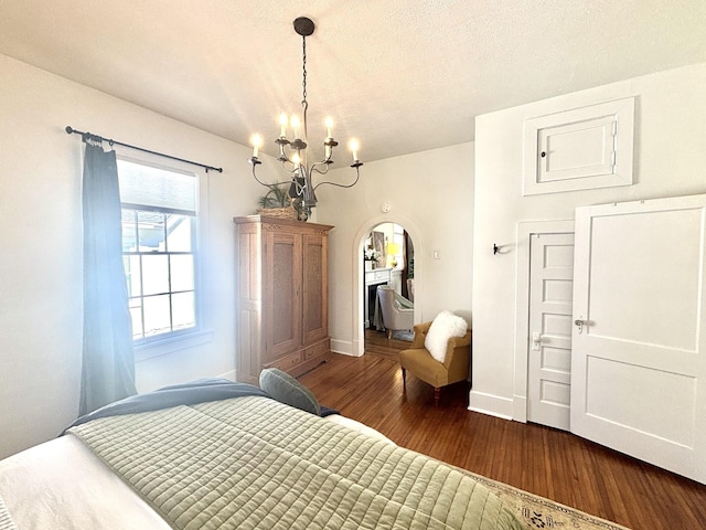 bedroom featuring baseboards, arched walkways, dark wood-type flooring, an inviting chandelier, and a textured ceiling