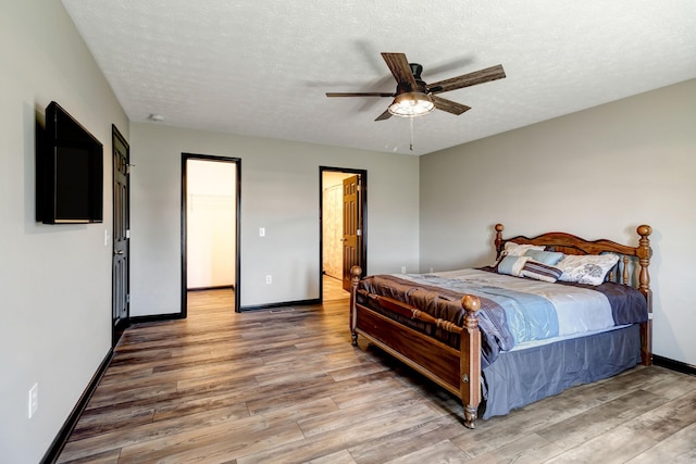 bedroom featuring ceiling fan, a textured ceiling, baseboards, and wood finished floors