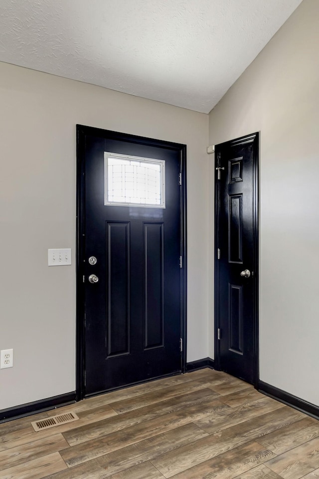 entrance foyer featuring baseboards, a textured ceiling, visible vents, and wood finished floors