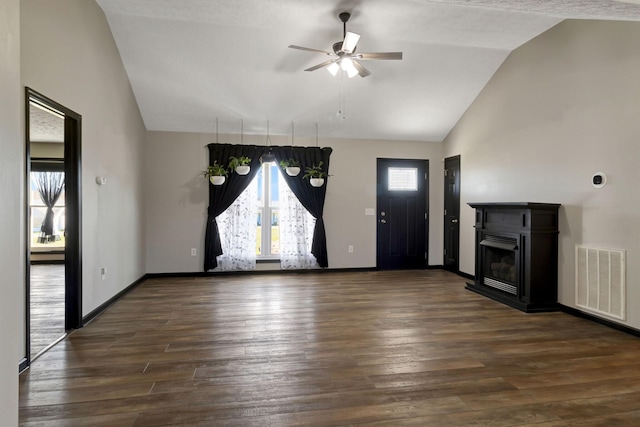 unfurnished living room with baseboards, a fireplace with raised hearth, visible vents, dark wood finished floors, and ceiling fan