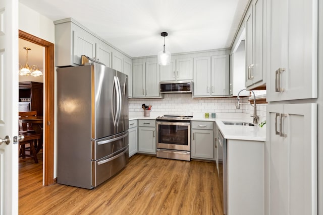 kitchen with light wood-style flooring, decorative backsplash, gray cabinetry, appliances with stainless steel finishes, and a sink