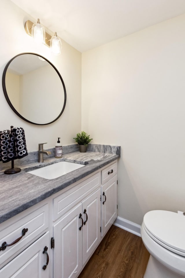 bathroom featuring toilet, baseboards, wood finished floors, and vanity