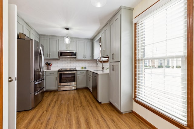 kitchen with tasteful backsplash, appliances with stainless steel finishes, wood finished floors, gray cabinets, and a sink