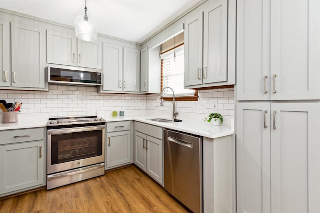 kitchen with tasteful backsplash, appliances with stainless steel finishes, gray cabinets, light wood-type flooring, and a sink