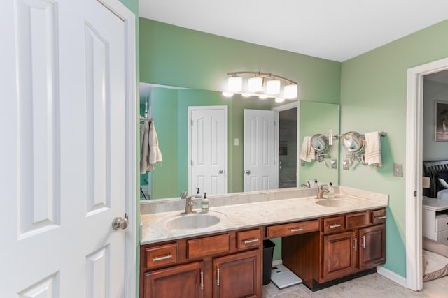 ensuite bathroom with baseboards, double vanity, a sink, and tile patterned floors