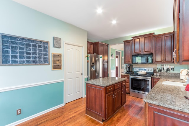 kitchen featuring light stone countertops, appliances with stainless steel finishes, a sink, and wood finished floors