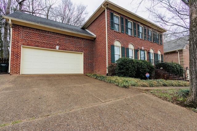 colonial inspired home featuring a garage, concrete driveway, and brick siding