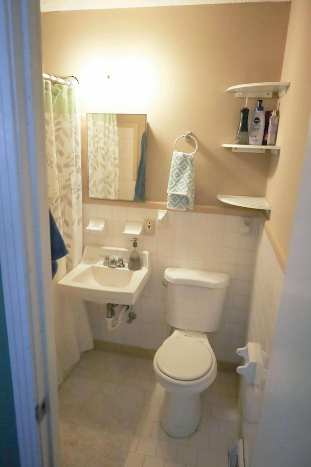 bathroom featuring toilet, a sink, tile walls, wainscoting, and tile patterned floors