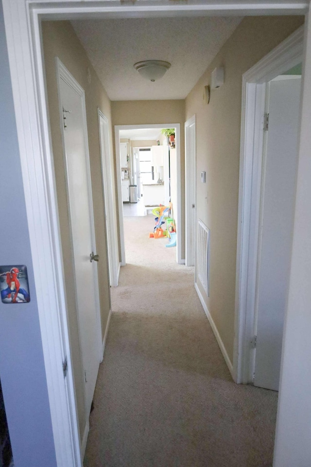 corridor featuring light colored carpet, visible vents, and baseboards