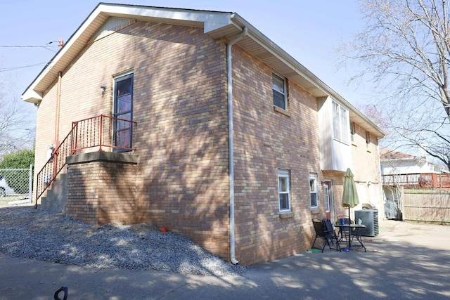 view of side of home featuring central air condition unit, brick siding, fence, and a patio