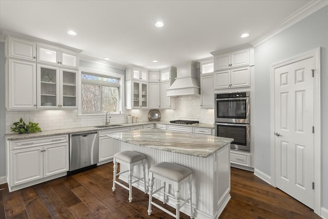 kitchen featuring dark wood finished floors, custom exhaust hood, appliances with stainless steel finishes, white cabinets, and a sink