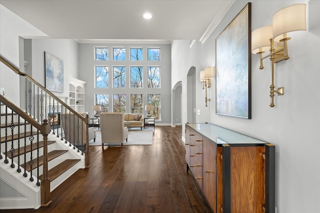 foyer entrance featuring baseboards, arched walkways, dark wood-style floors, stairway, and a high ceiling