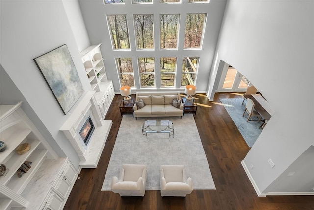 living room featuring a glass covered fireplace, a towering ceiling, baseboards, and wood finished floors