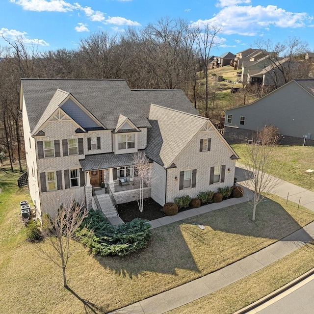 view of front of home with covered porch, driveway, a front lawn, and roof with shingles