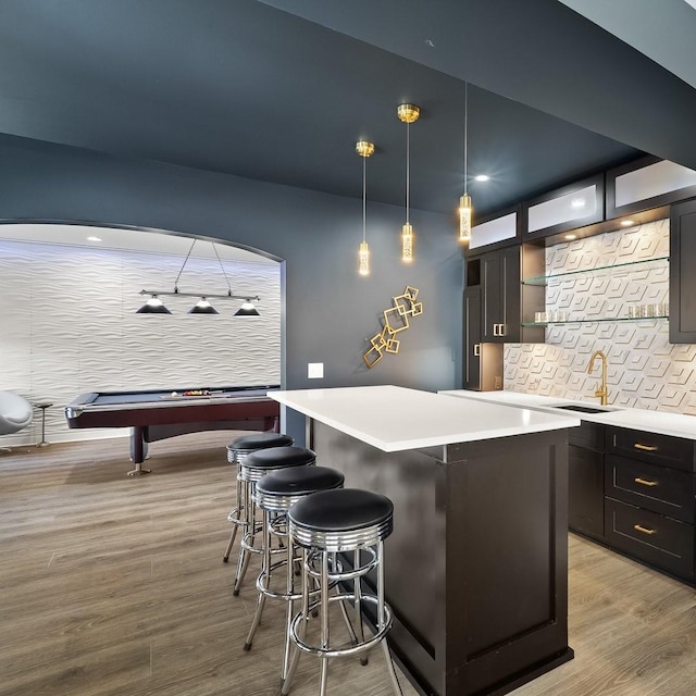 bar featuring decorative backsplash, a sink, hanging light fixtures, and light wood finished floors