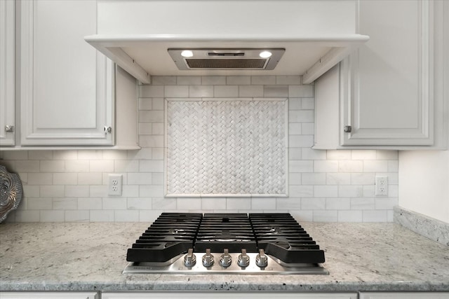 kitchen with extractor fan, stainless steel gas stovetop, light stone counters, and decorative backsplash