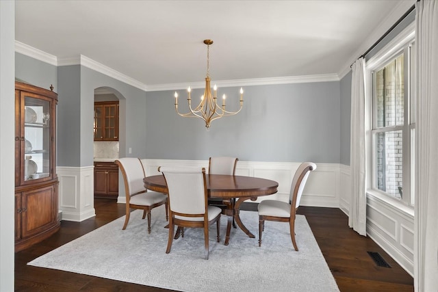 dining room with dark wood-style floors, arched walkways, visible vents, ornamental molding, and wainscoting