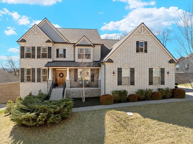 view of front of property with covered porch, a front lawn, and brick siding