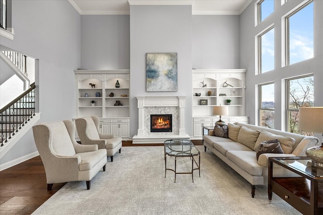 living area featuring a towering ceiling, wood finished floors, stairs, crown molding, and a high end fireplace