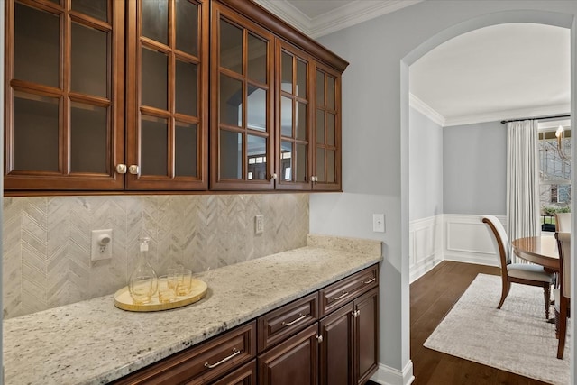 kitchen with light stone counters, arched walkways, dark wood finished floors, crown molding, and glass insert cabinets