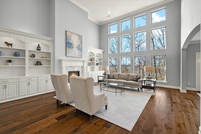 living area with arched walkways, dark wood finished floors, crown molding, and a high end fireplace